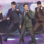 Korean trot singer performing on stage in a glittering suit with dramatic lighting.