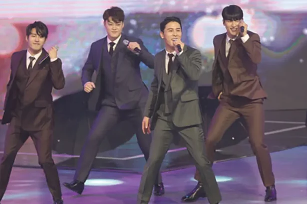 Korean trot singer performing on stage in a glittering suit with dramatic lighting.