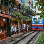 Tourists on Hanoi’s Train Street watch a train pass dangerously close among colorful lanterns and cafes