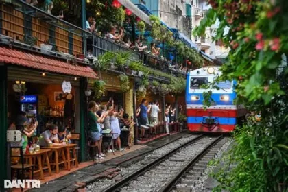 Tourists on Hanoi’s Train Street watch a train pass dangerously close among colorful lanterns and cafes