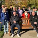 Solar-lit wooden mental health bench in a UK park with supportive message carved into it