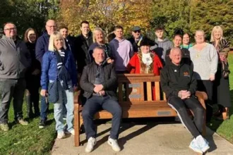 Solar-lit wooden mental health bench in a UK park with supportive message carved into it