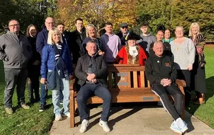 Solar-lit wooden mental health bench in a UK park with supportive message carved into it
