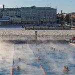 Person ice bathing in a frozen Finnish lake near a wooden sauna