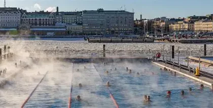 Person ice bathing in a frozen Finnish lake near a wooden sauna