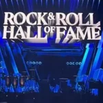 Oasis band members performing live on stage with a large crowd in the background.