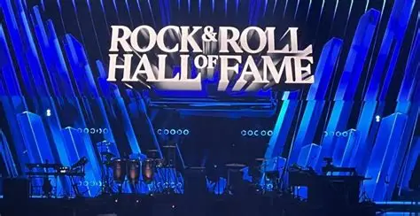 Oasis band members performing live on stage with a large crowd in the background.