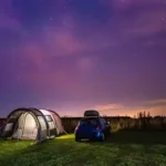 Person sleeps peacefully in tent under starry sky with campfire glow, surrounded by forest embodying natural circadian rhythm reset.