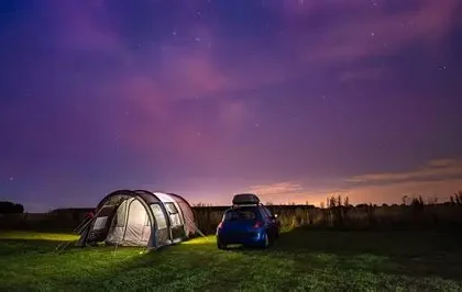 Person sleeps peacefully in tent under starry sky with campfire glow, surrounded by forest embodying natural circadian rhythm reset.