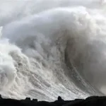 Wind-swept UK coastal town battered by storm waves under dark skies, illustrating named weather events like Chandra.