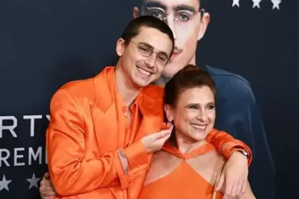 Timothée Chalamet speaking at a public event with a theatre stage in the background.