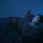 Person using smartphone at night with dim lighting affecting sleep patterns