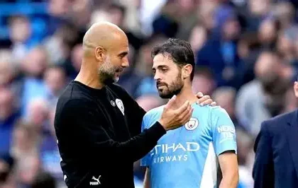 Manchester City captain Bernardo Silva celebrates EFL Cup win as Pep Guardiola watches intently from touchline.