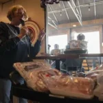 Excited winner grabs wrapped meat prizes including steaks and pork chops at Minnesota meat raffle event.