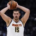 Nikola Jokic drives past Victor Wembanyama in intense Nuggets-Spurs overtime battle, crowd roaring in background.
