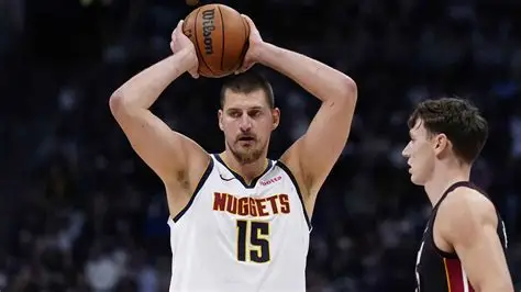 Nikola Jokic drives past Victor Wembanyama in intense Nuggets-Spurs overtime battle, crowd roaring in background.