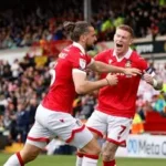 Wrexham owners Ryan Reynolds and Rob McElhenney celebrate with fans at Championship match amid promotion push.