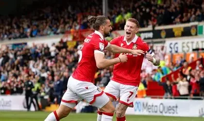Wrexham owners Ryan Reynolds and Rob McElhenney celebrate with fans at Championship match amid promotion push.