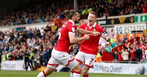 Wrexham owners Ryan Reynolds and Rob McElhenney celebrate with fans at Championship match amid promotion push.