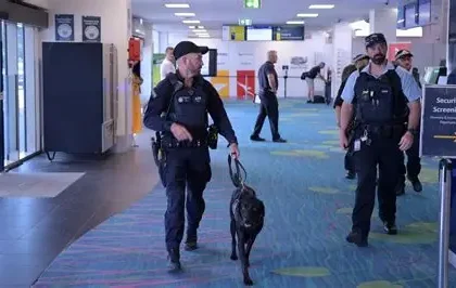 A CBP K9 officer and chocolate Labrador retriever currency detection dog at an airport security checkpoint during an outbound enforcement operation.