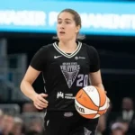 A WNBA player in a Golden State Valkyries uniform dribbling the basketball during a pre-season game, with arena crowd visible in the background.