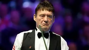 Snooker legend Jimmy White holding a cue at a snooker tournament, smiling at the camera.